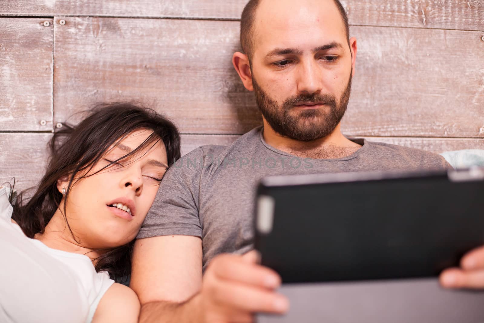 Beautiful wife sleeping on her husband husband while he is working late on tablet computer.