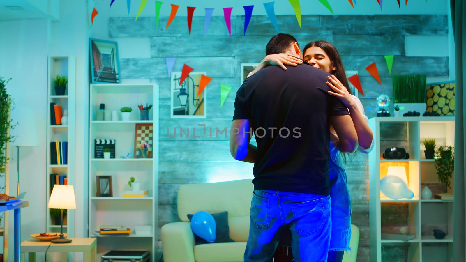 Attractive bearded young man dancing on romantic music with his girlfriend in a room with neon lights. Care free couple.