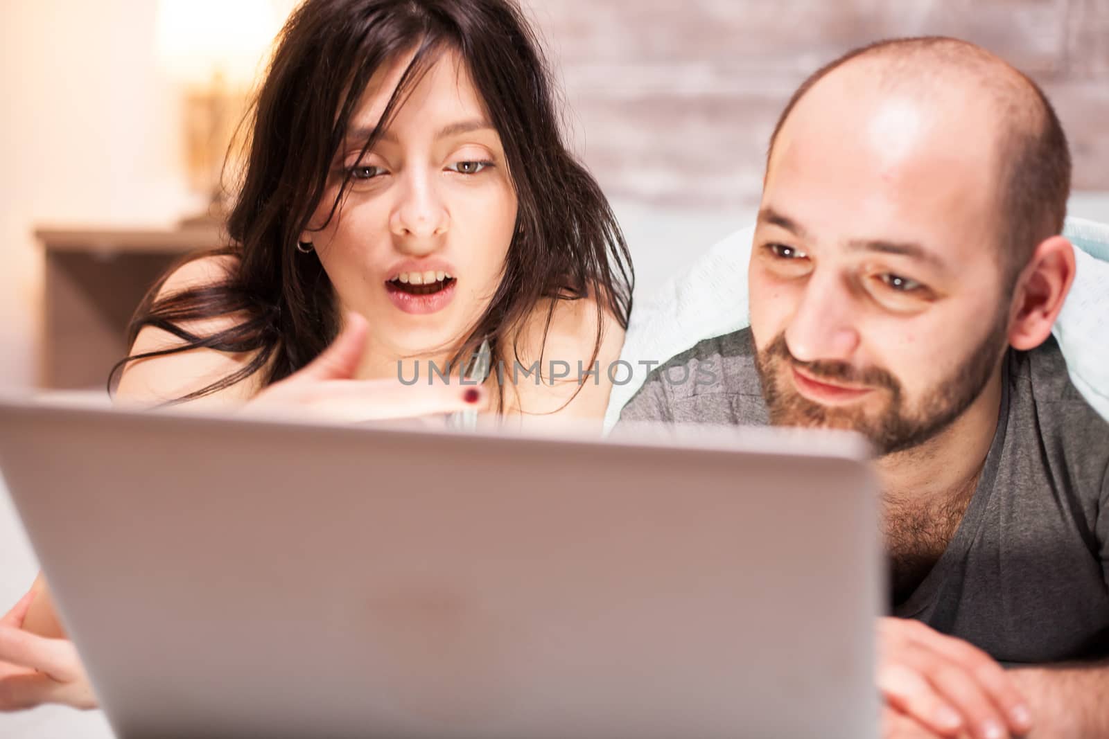 Close up of shocked wife in pajamas while watching a movie on laptop with her husband.