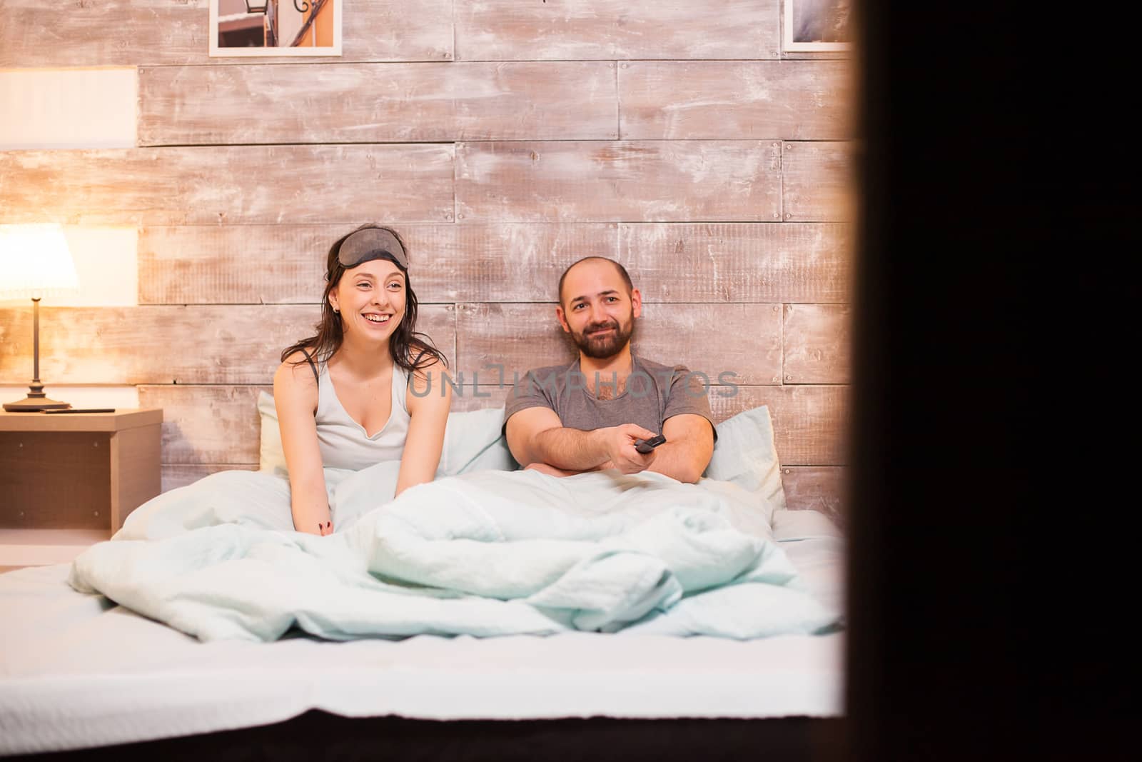 Cheerful couple in pajamas watching a comedy movie by DCStudio