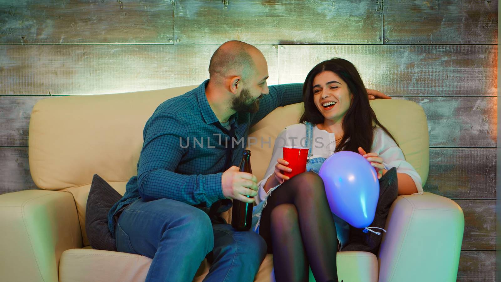 Handsome young man making beautiful girl laugh at his best friend party. Drinking alcohol.