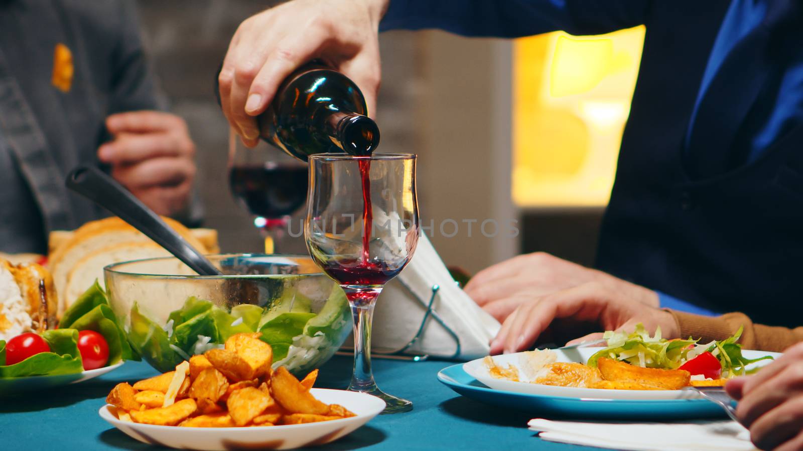 Zoom in shot of young man pouring red wine into a glass at family dinner.