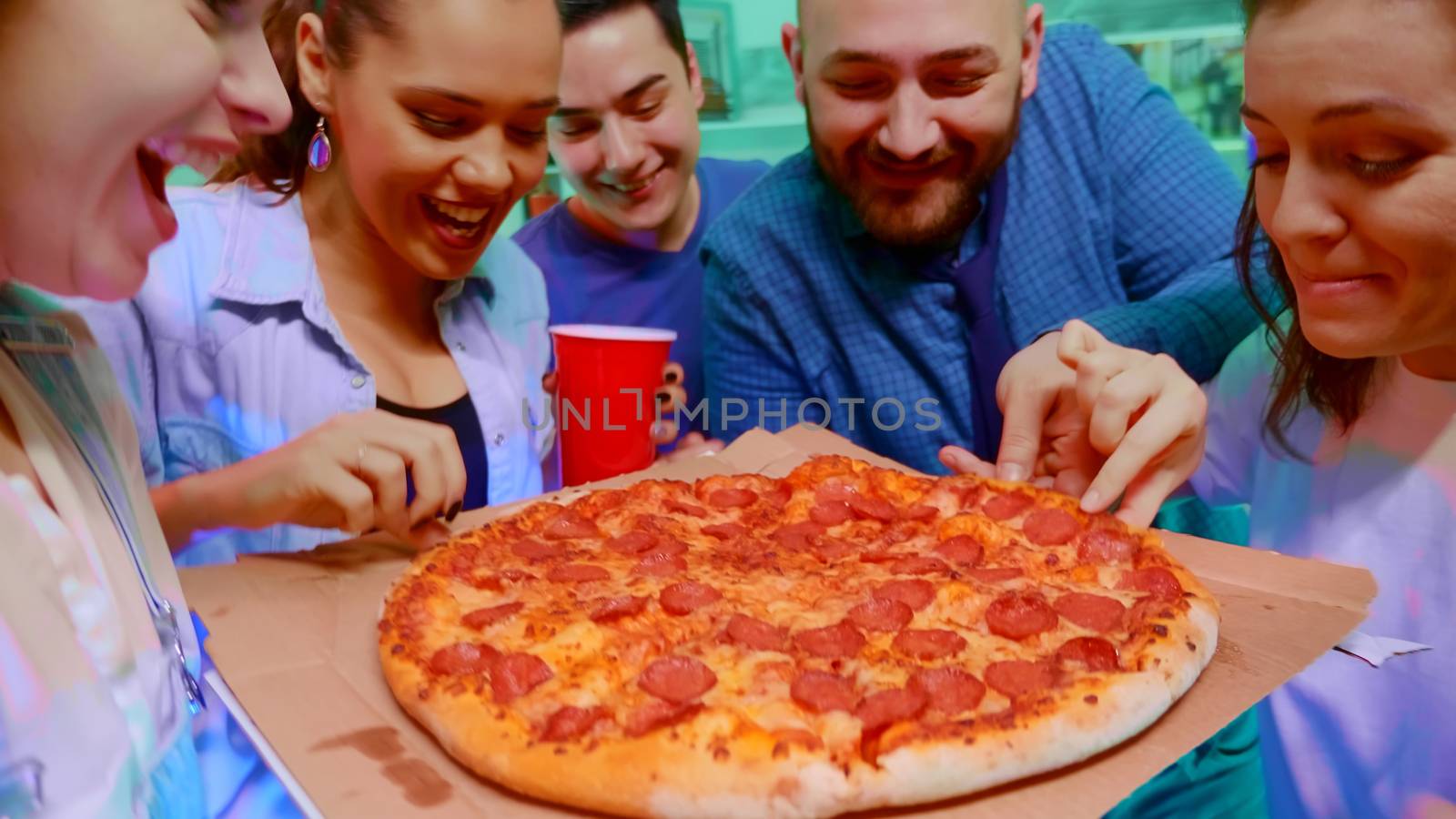 Follow shot of girl arriving at the party with delicious pizza for her friends. Excited group of people.