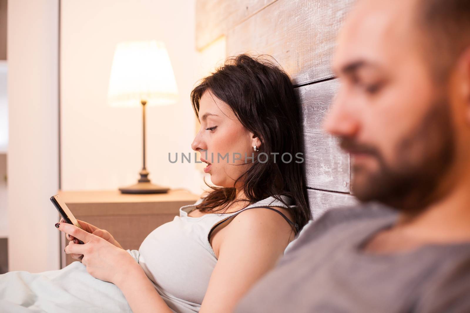 Beautiful wife wearing pajamas using her mobile phone and having a conversation with her husband.