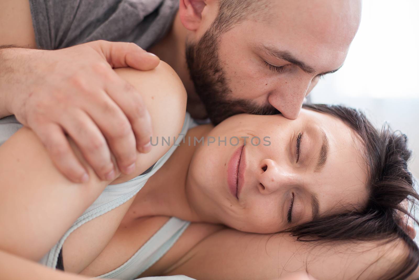 Wife smiling in her sleep while the husband is kissing her cheek.