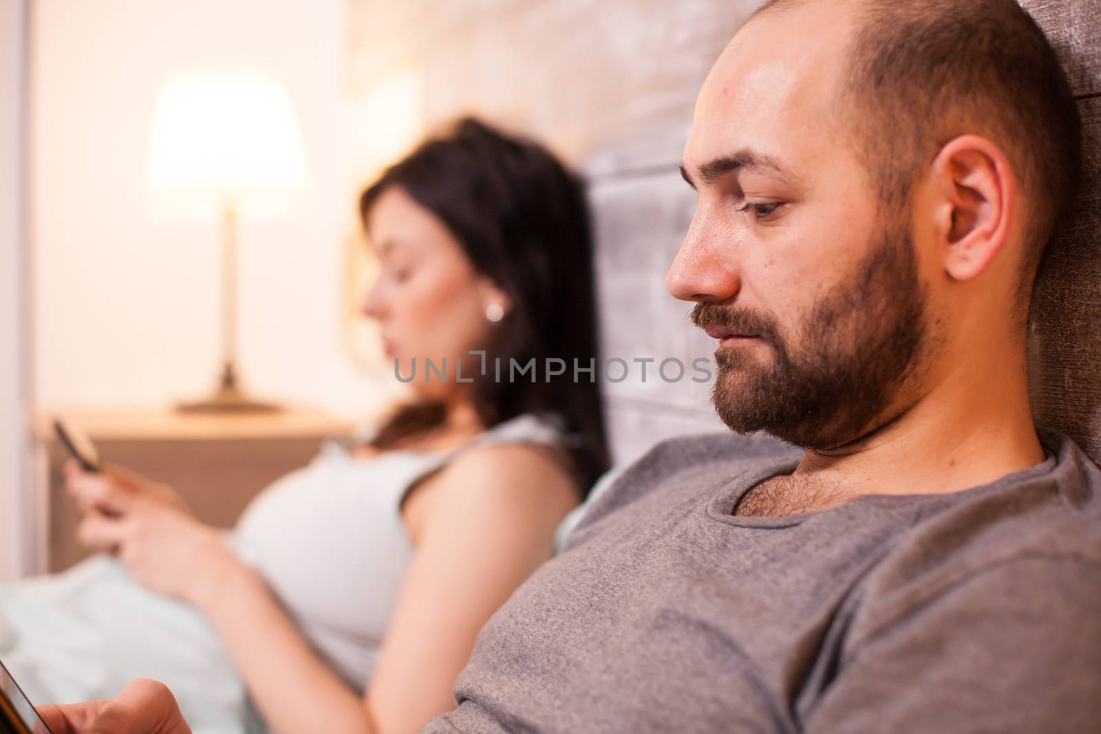 Man reading in bed with wife by DCStudio