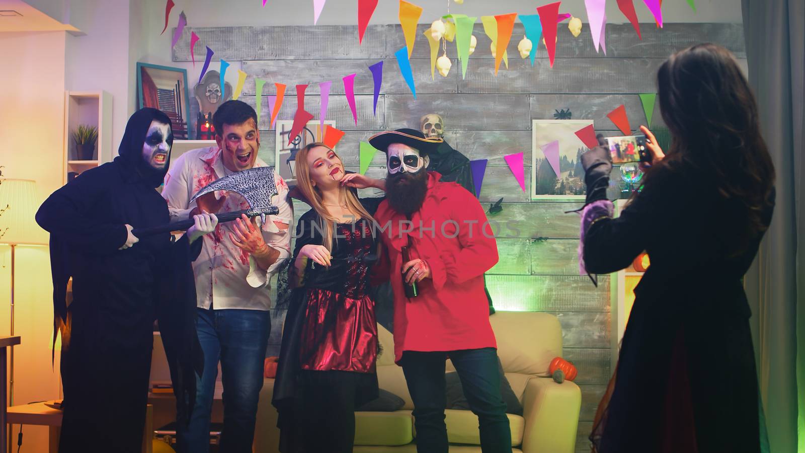 Spooky witch taking photos of her scary friends while celebrating halloween in a decorated house