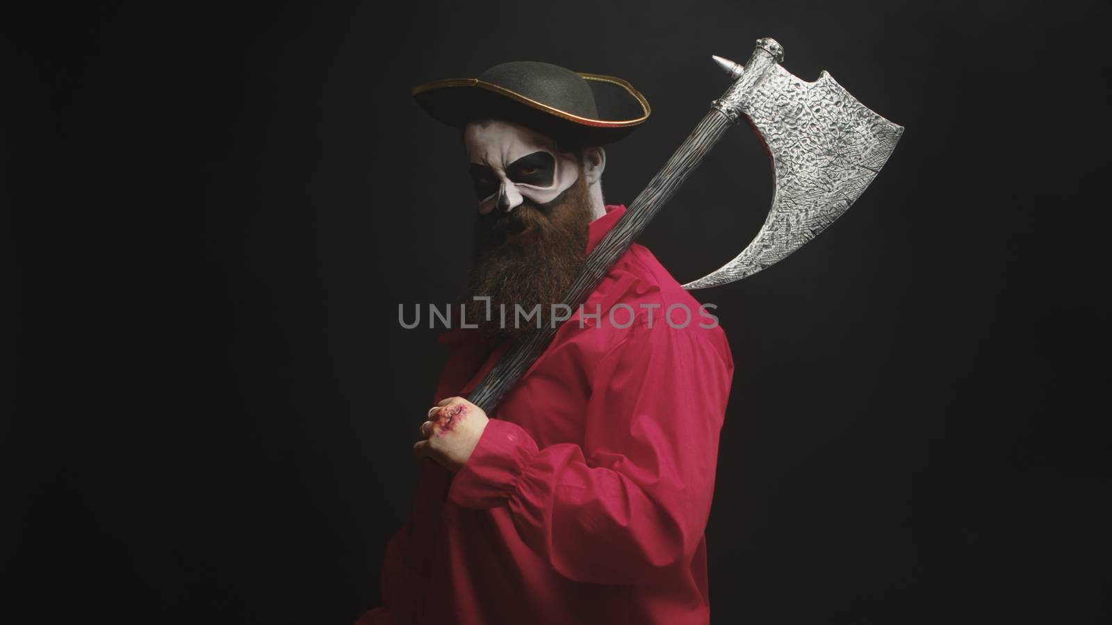 Scary bearded man holding an axe dressed up like a pirate for halloween.