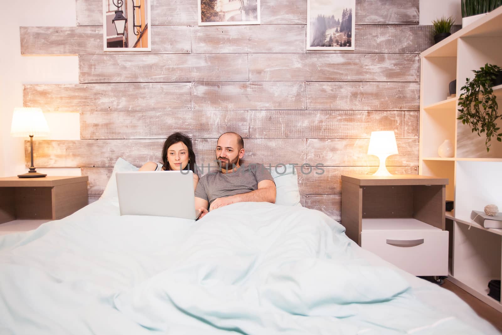 Husband and wife wearing pajamas working late on laptop before bedtime.