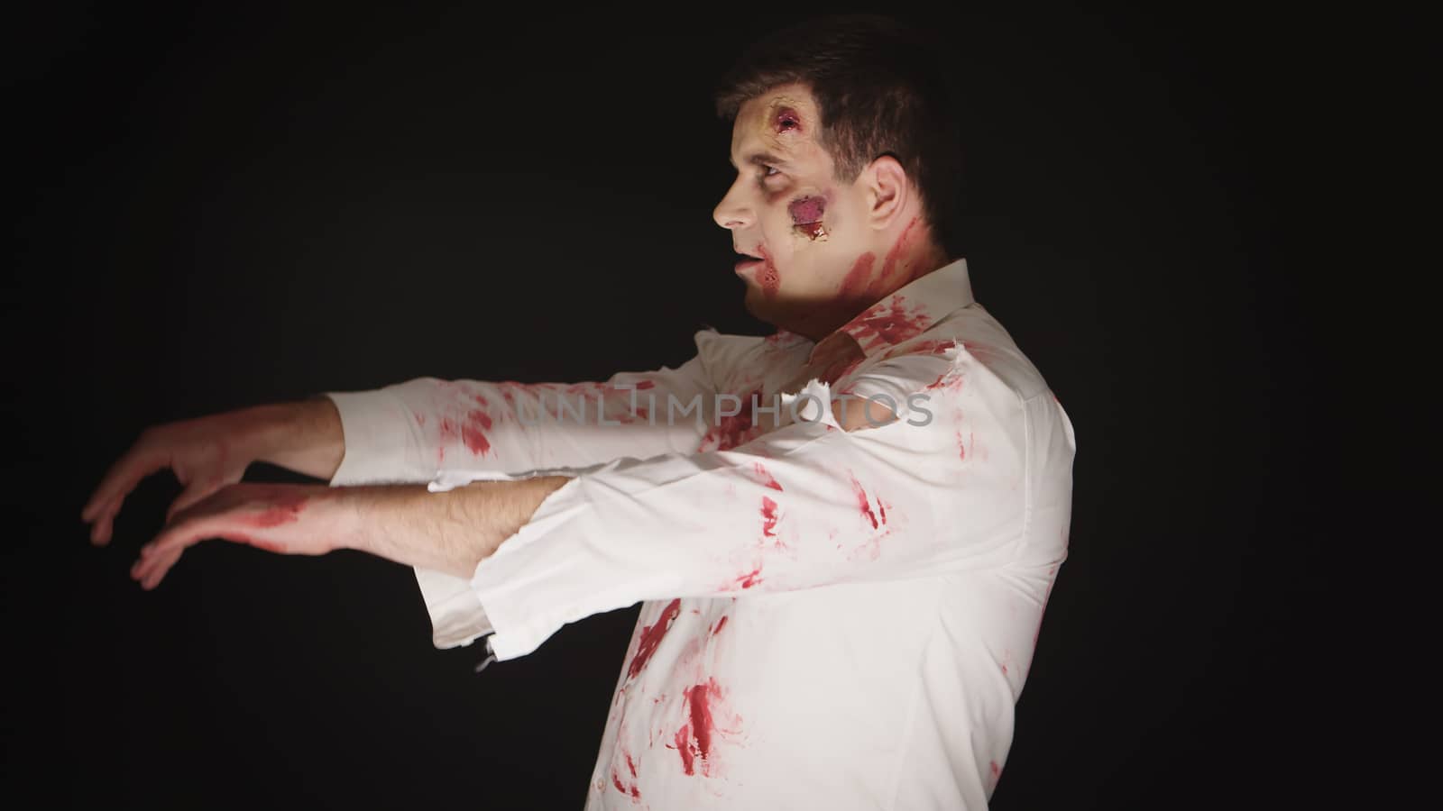 Guy dressed up like a zombie for halloween with blood and scars over black background.