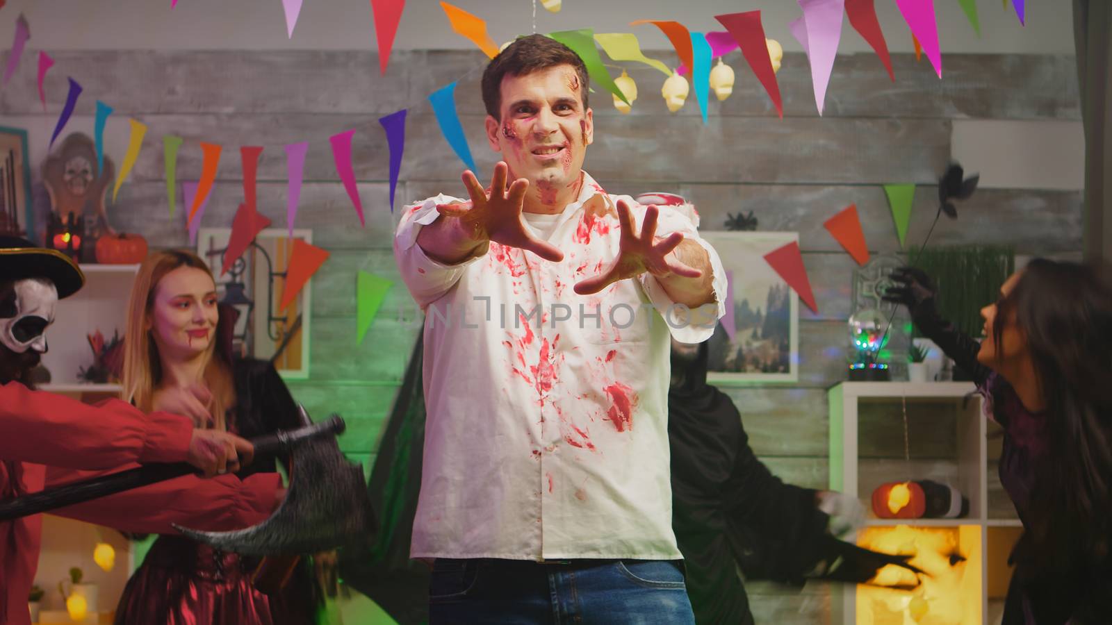 Adult man disguised like a scary zombie with professional make up at halloween party with his friends in a decorated house.