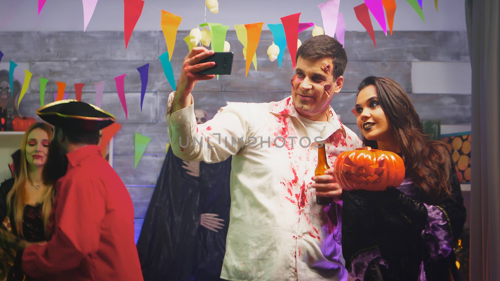 Spooky zombie taking a selfie with beautiful witch woman at halloween party.