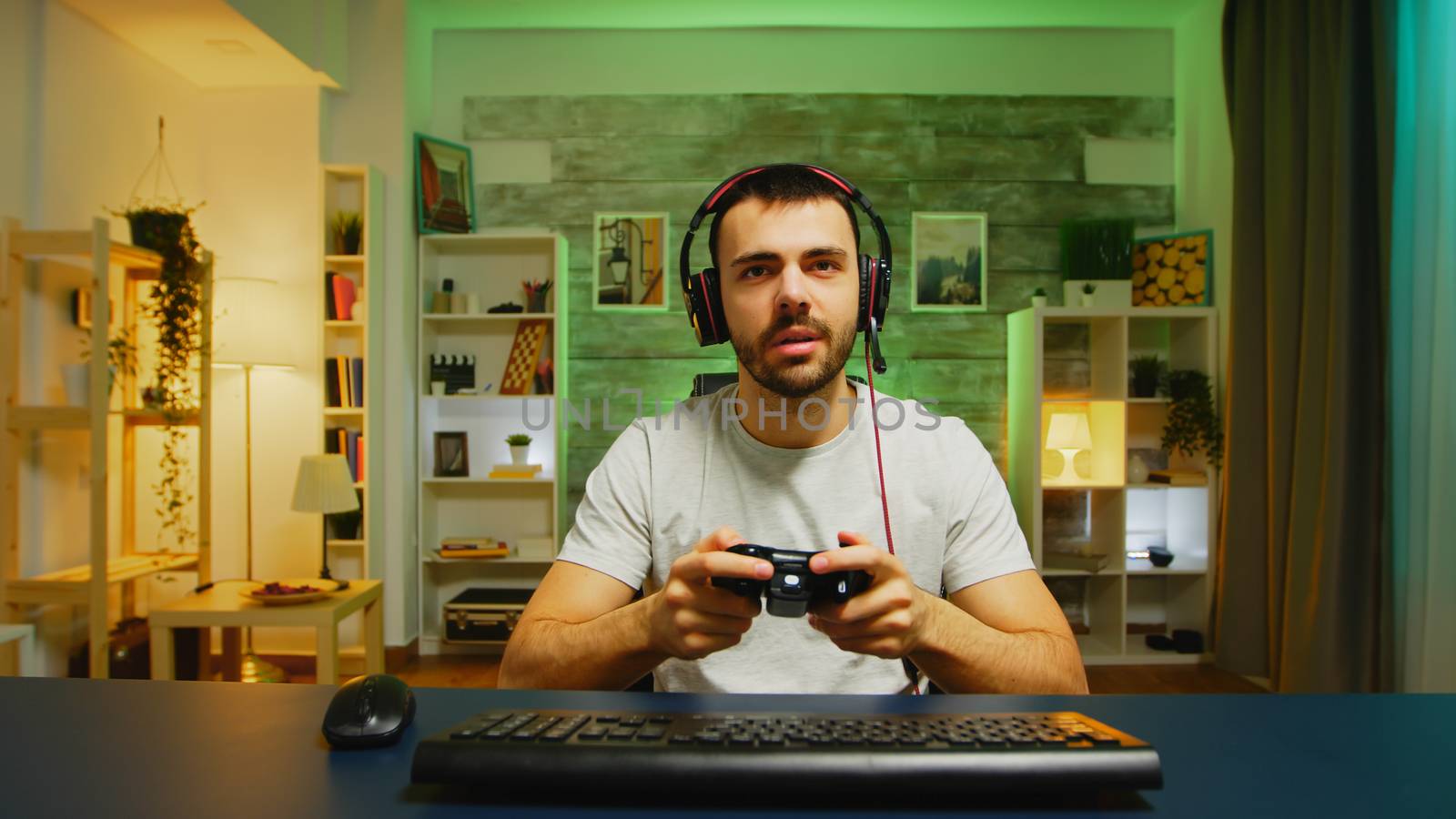 Pov of young man with headphones in in a room with neon light playing games with wireless controller.