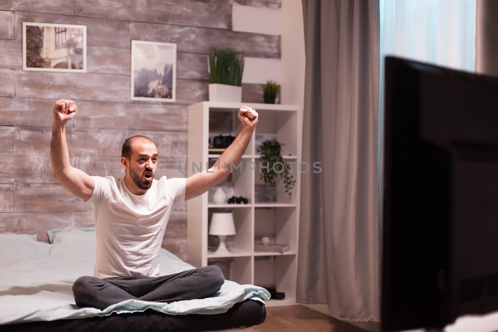 Excited sports fan in bed by DCStudio