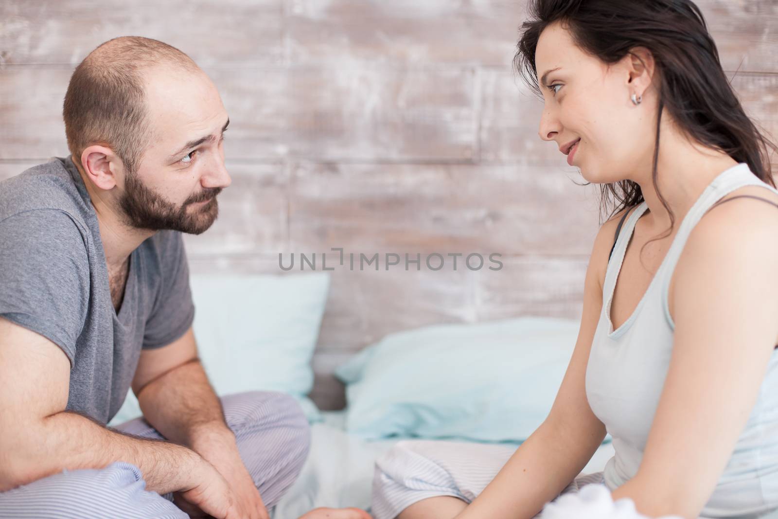 Husband and wife wearing pajamas looking at each other after waking up in the morning.