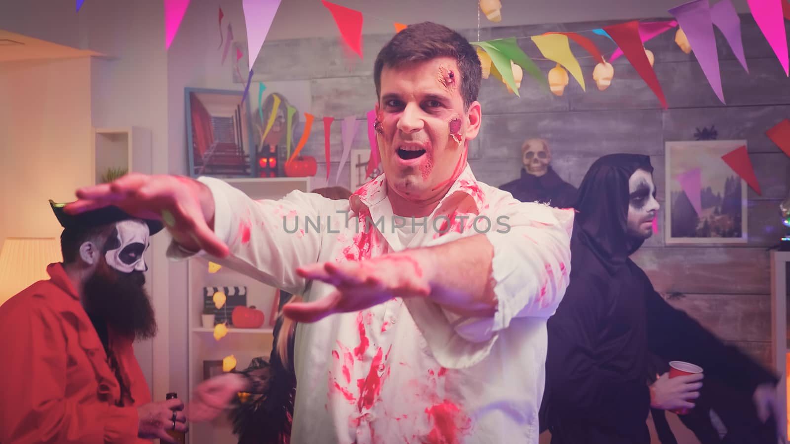 Scary and dangerous zombie at halloween party having fun and dancing next to his disguised friends