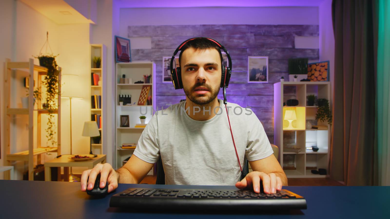Pov young man talking with other players using headphones with microphone while playing games on powerful PC.