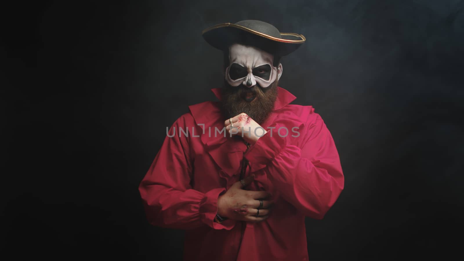 Man dressed up like a scary pirate in red shirt and with a hat for halloween over black background.