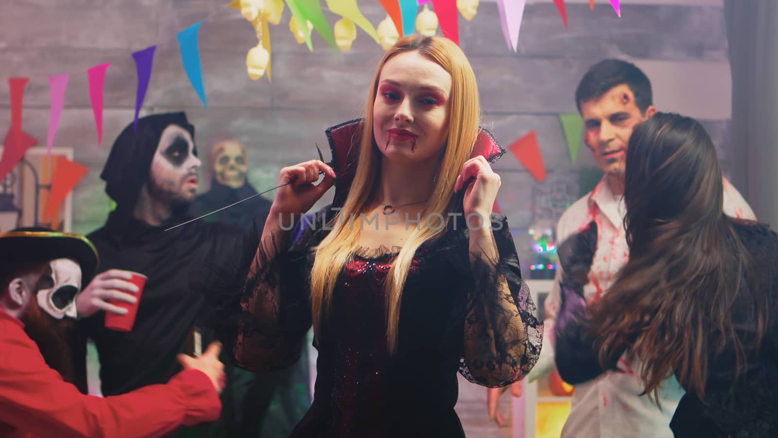 Attractive blonde woman dressed up like sexy witch for halloween party with her friends dressed up like different monsters.