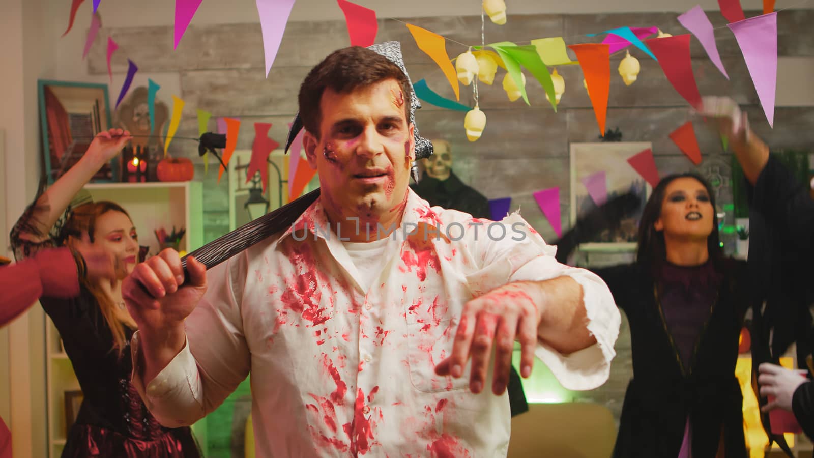 Adult man disguised as a zombie with an axe at halloween party.