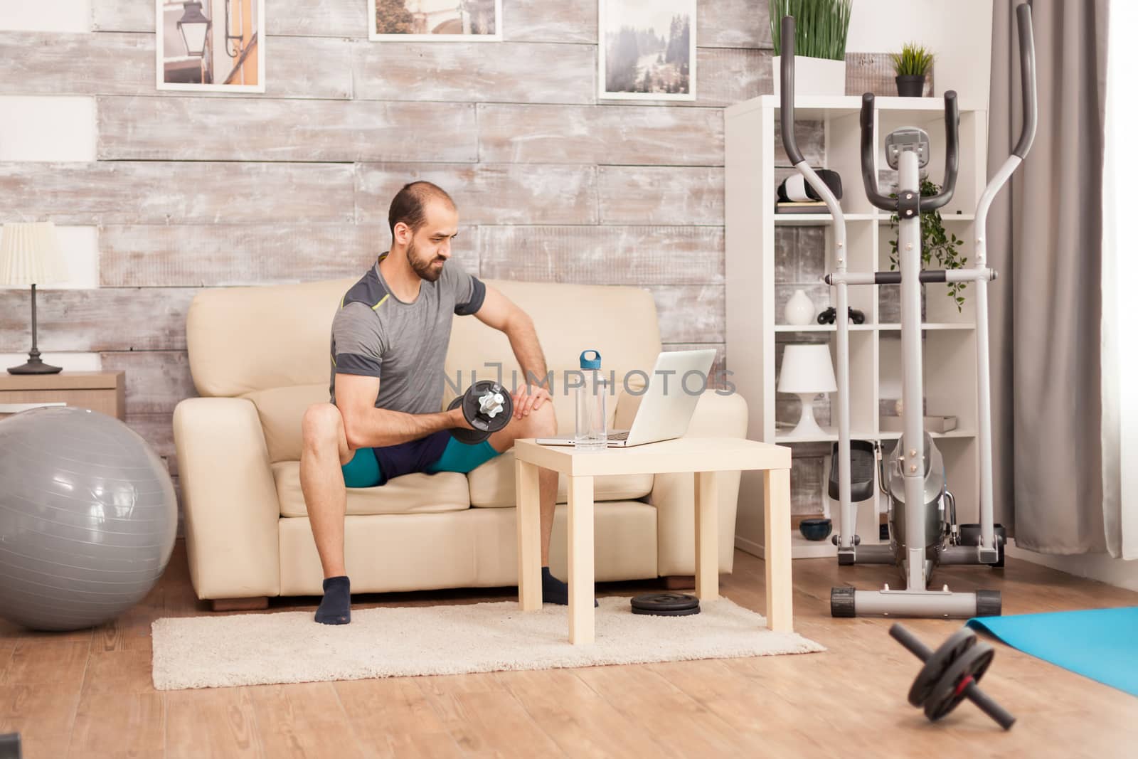 Fit man on sofa training biceps with dumbbell by DCStudio