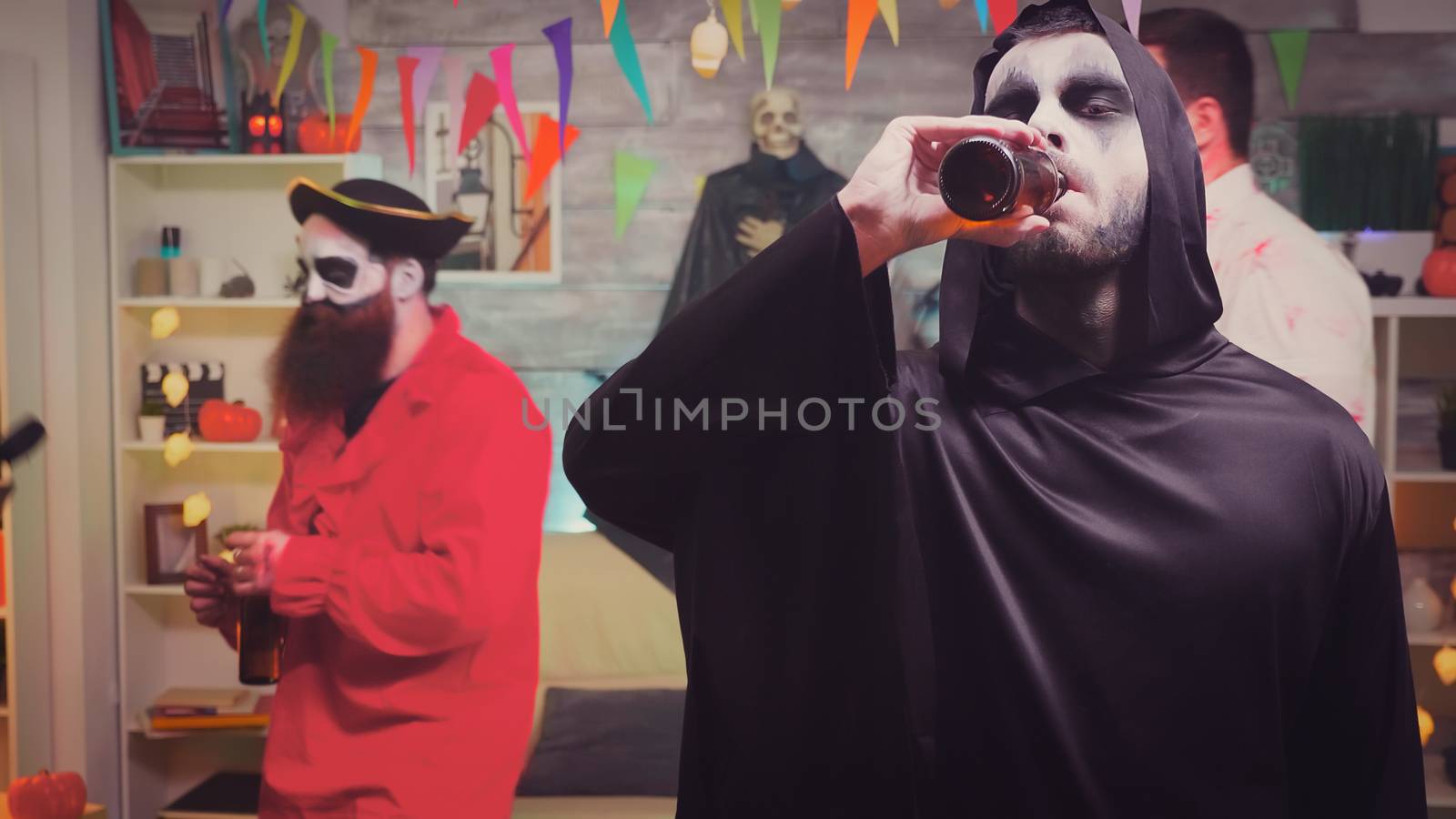 Zoom in shot of man dressed up like grim reaper drinking beer at halloween party.