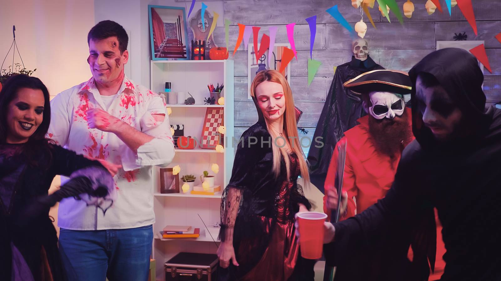 Group of young people disguise in spooky characters at halloween party having fun and dancing in decorated room