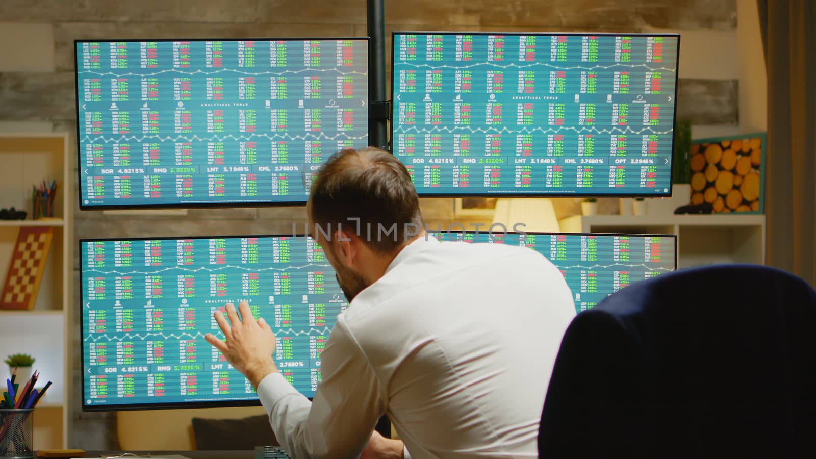 Bearded trader in his home office wearing a suits checking the stock market on four displays