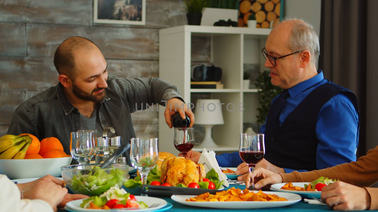 Young man serving his father in law with red wine at family lunch. Delicious food.