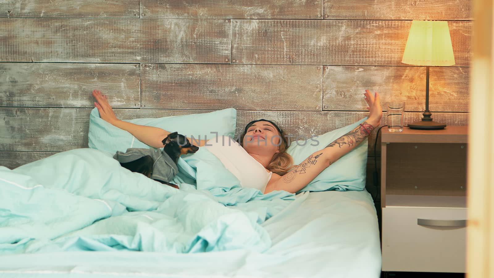 Beautiful young woman in pajamas taking off her sleep mask while waking up. Happy dog.
