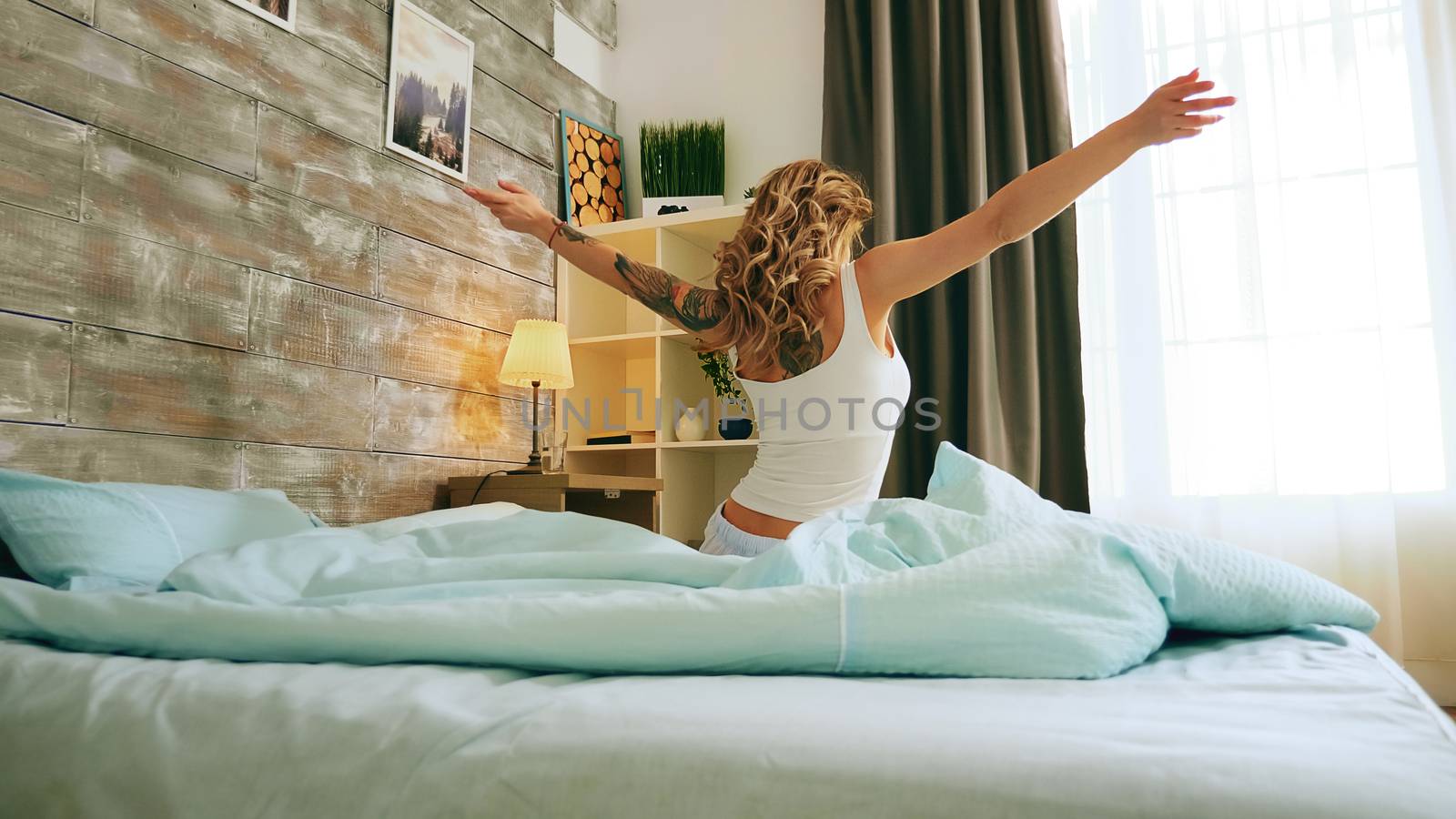 Back view of beautiful woman stretching out after waking up early in comfortable bed.