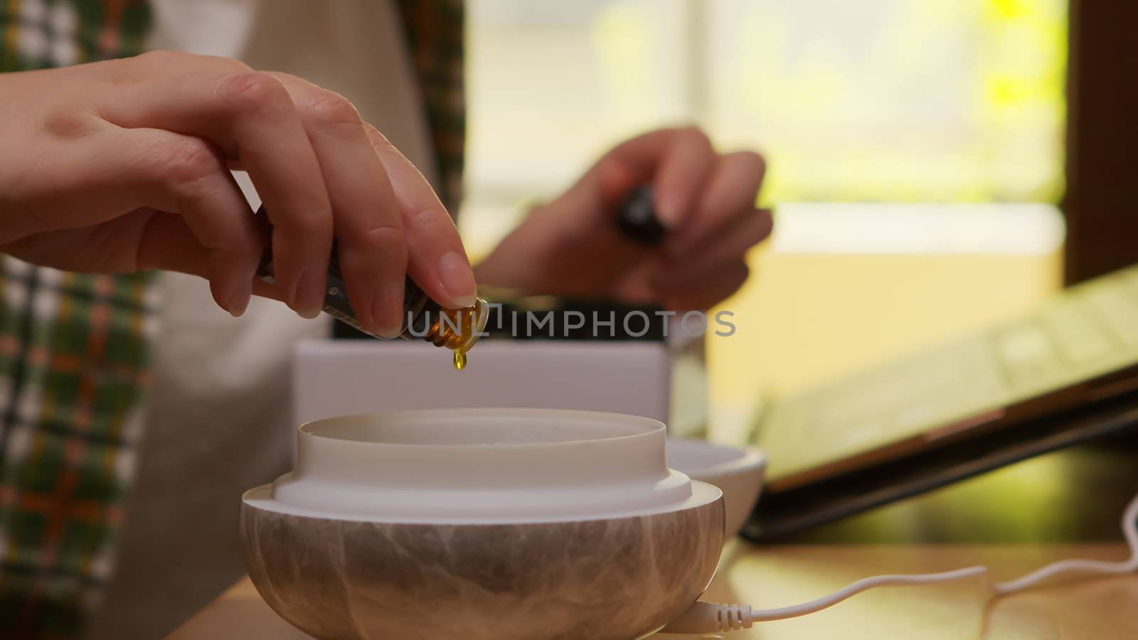 Woman adds essential oil into diffuser in kitchen