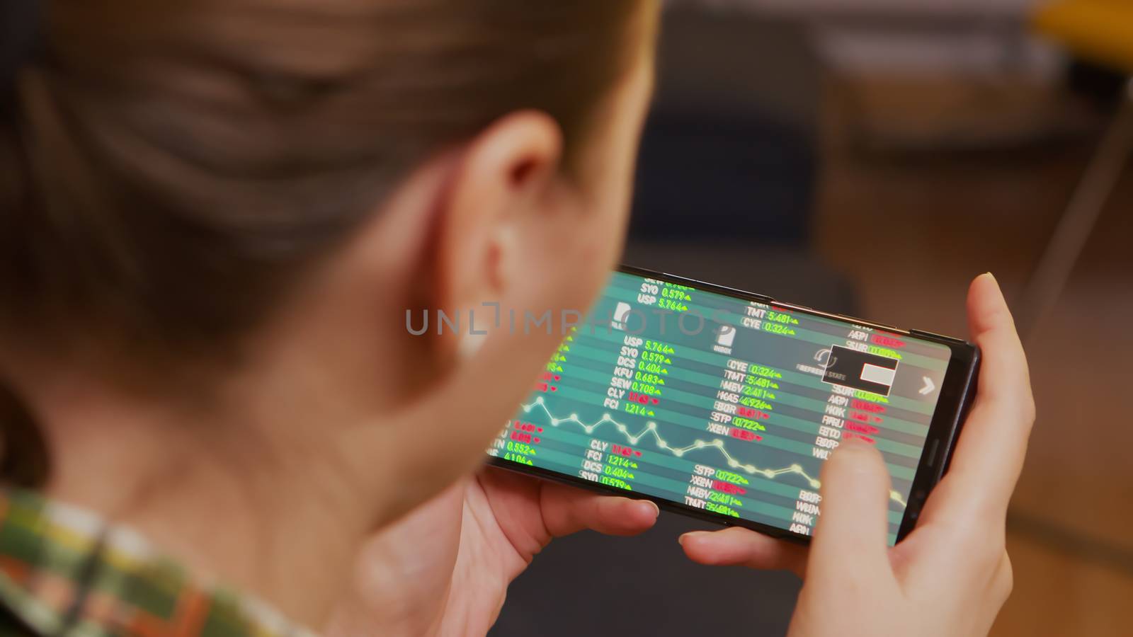 Back view of woman checking stock trading using smartphone.