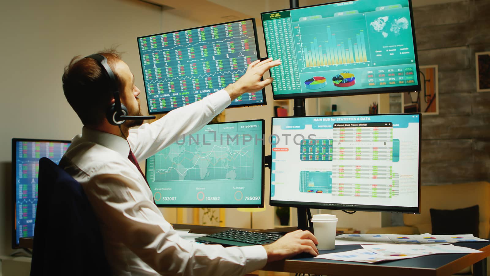 Overworked stock market trader drinking coffee in home office in front of multiple displays with real time data analysis.