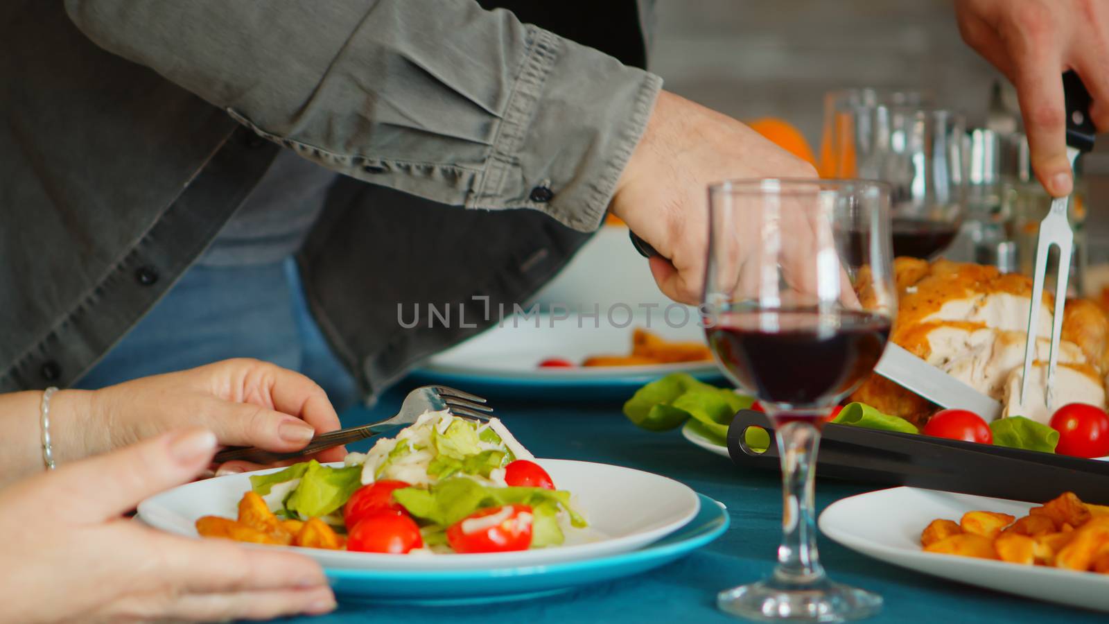 Close up of young man serving his mother with a slice of roasted chicken at family dinner.