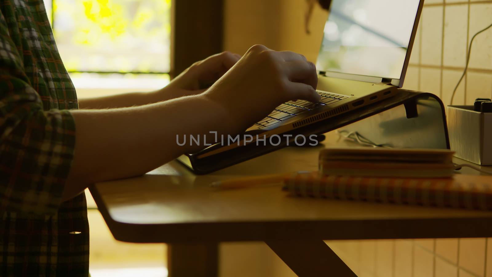 Female freelance in silhouette working on laptop from home in casual clothes.