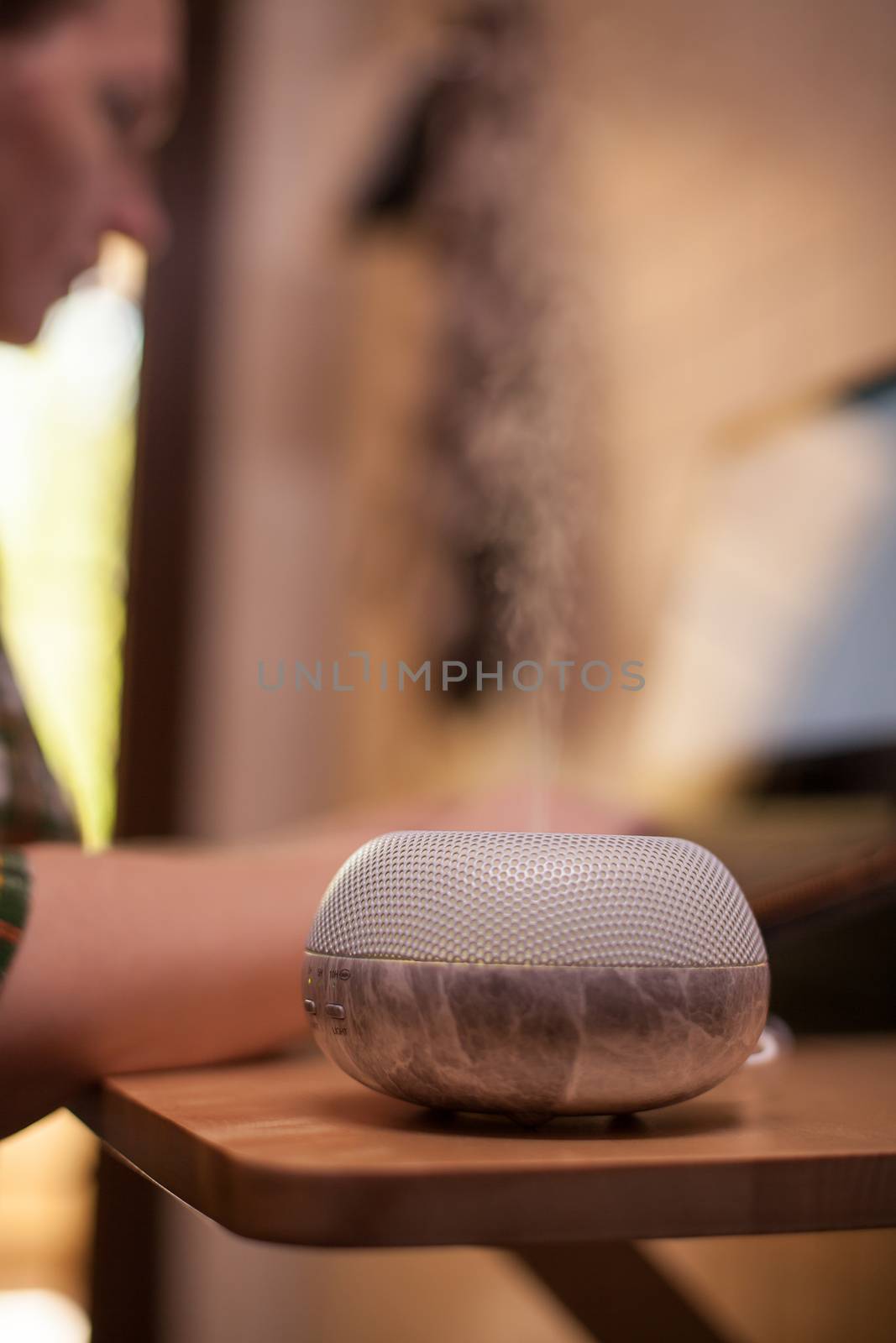 Essential oil diffuser with young woman working on laptop in the background.