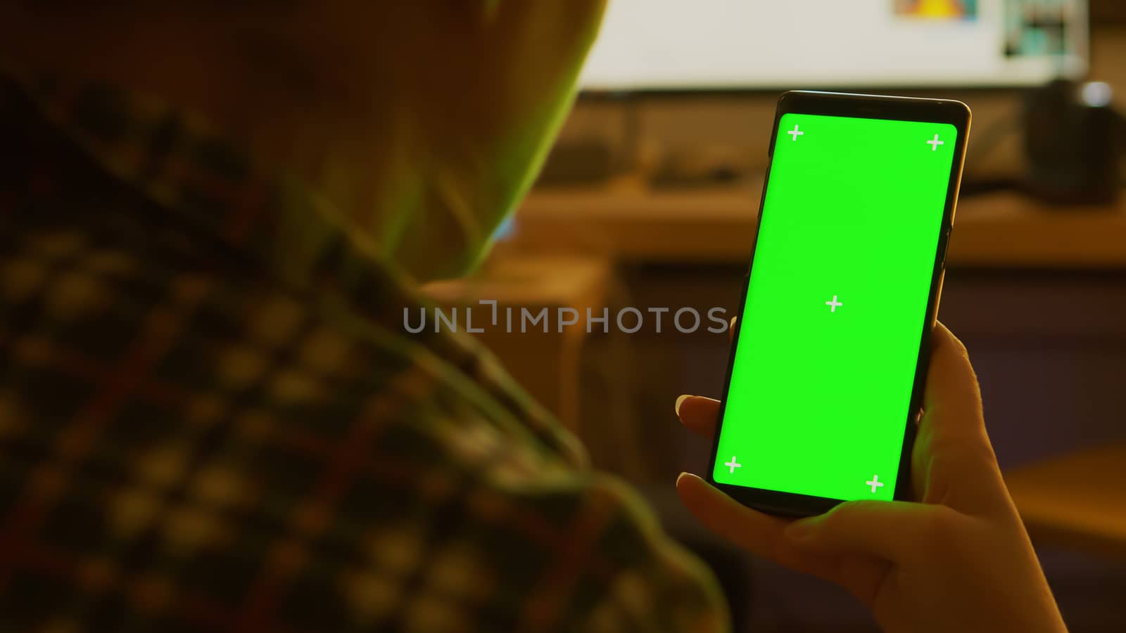 Back view of young woman holding smartphone with green screen.