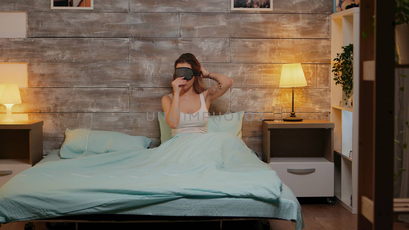 Beautiful woman in pajamas using her phone before going to sleep. Sleep mask.