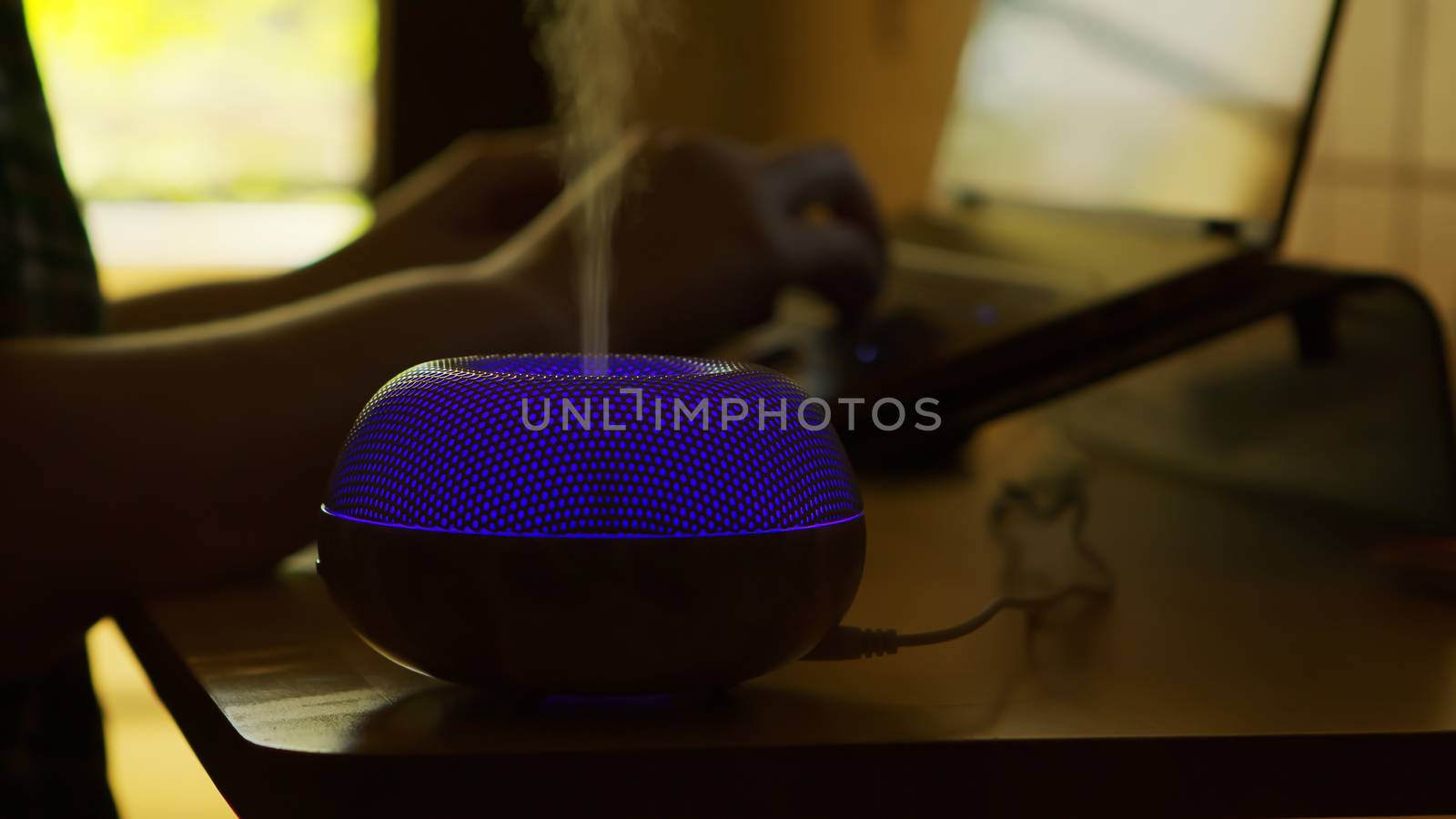 Blue led light aroma oil diffuser on table and freelancer woman working from home in the background.