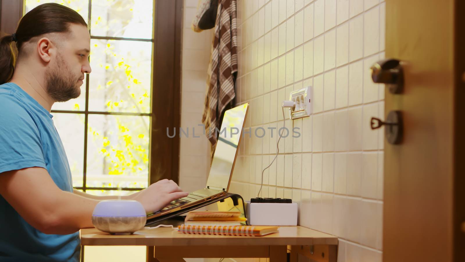 Freelancer working on laptop in his kitchen while a small essential oil diffuser is steaming next to him