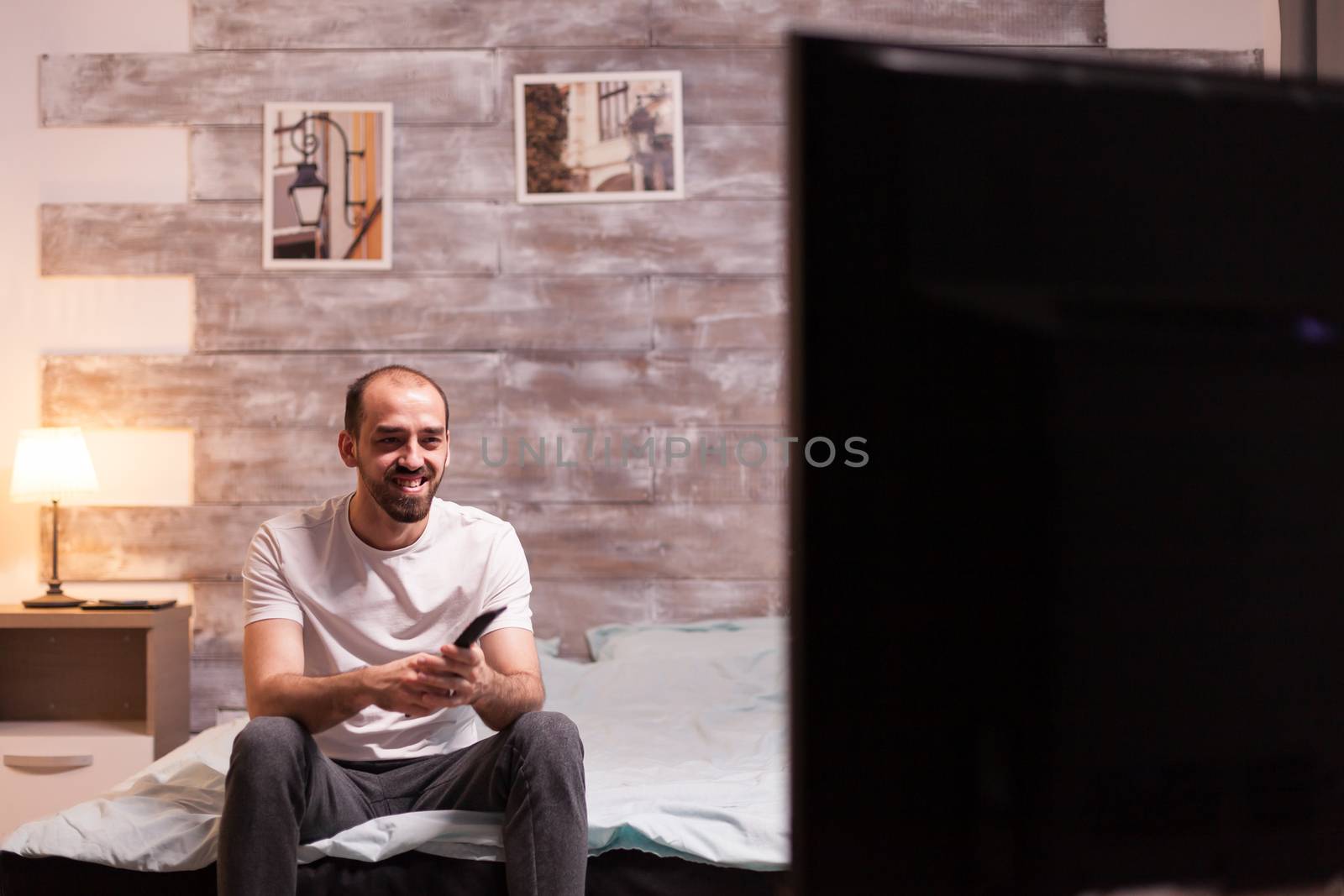 Man with a big smile holding remote control while watching tv at night.