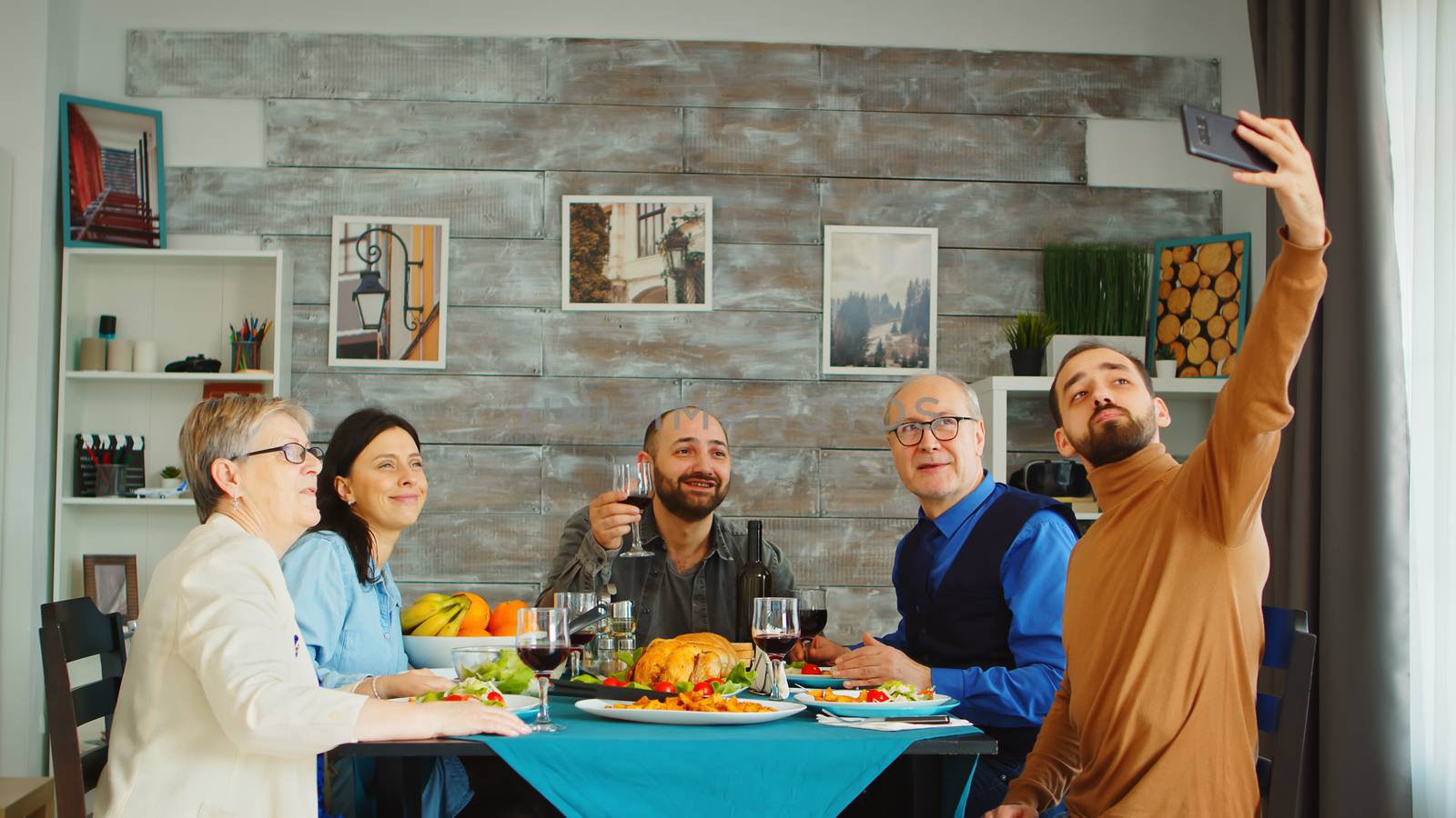 Handsome bearded man using his smartphone to take a selfie with his family at dinner.