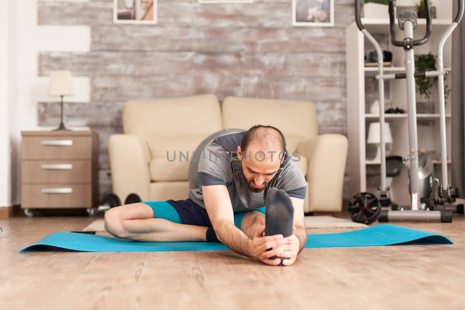 Athletic man stretching out before workout on yoga mat in home during global pandemic.