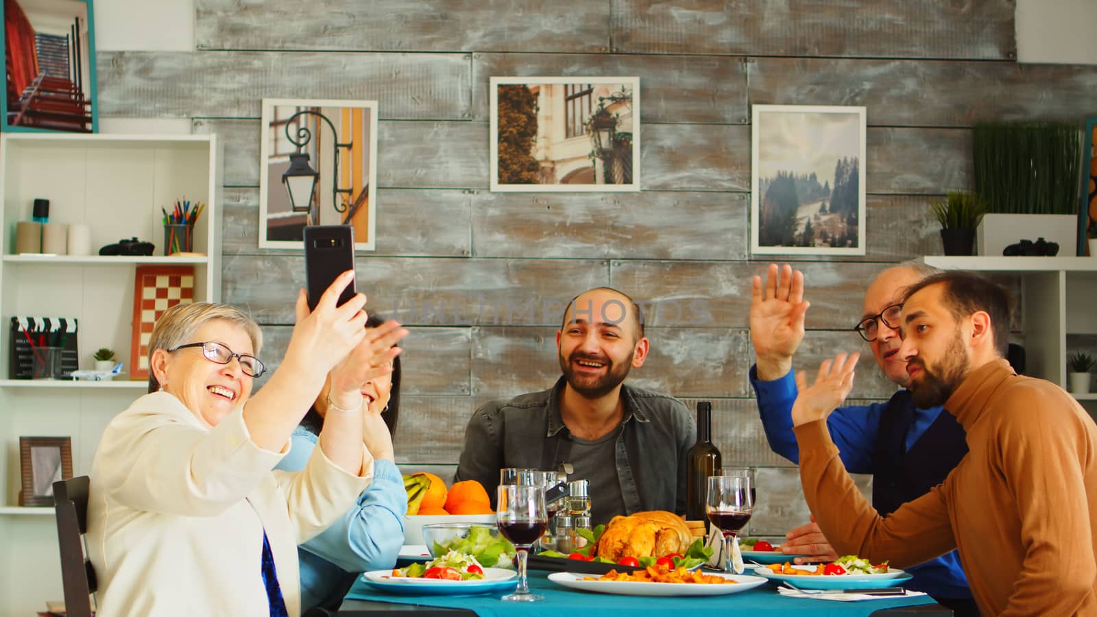 Cheerful family laughing while video call chatting from phone at dinner.