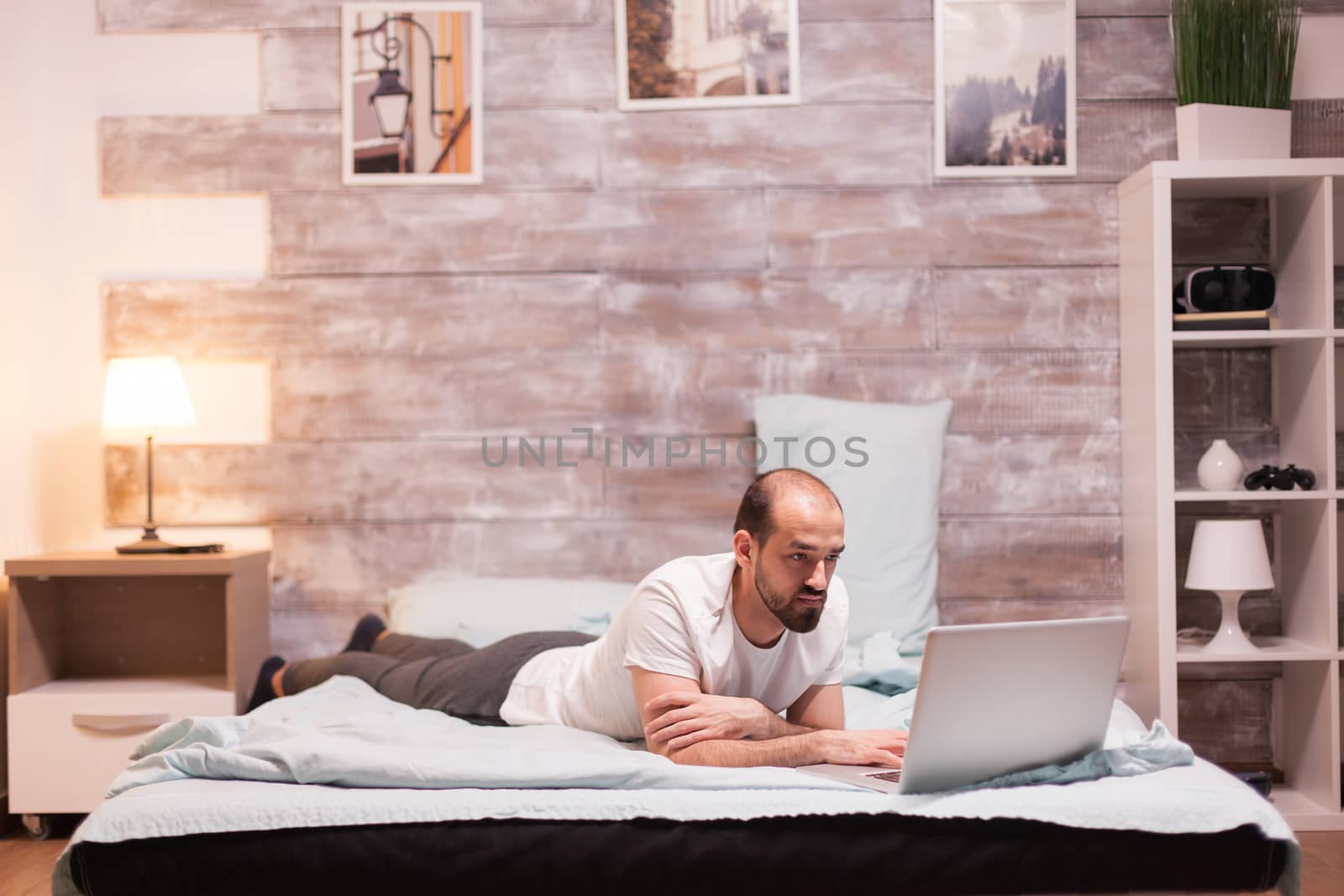 Man browsing on laptop at night in bed wearing pajamas.