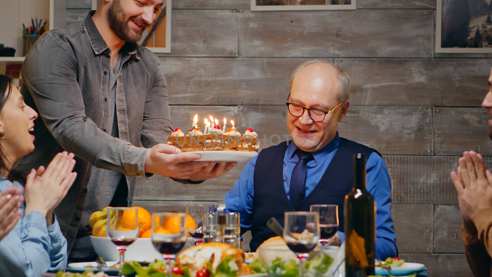 Senior man celebrating his birthday with the family. Delicious cake. Slow motion shot