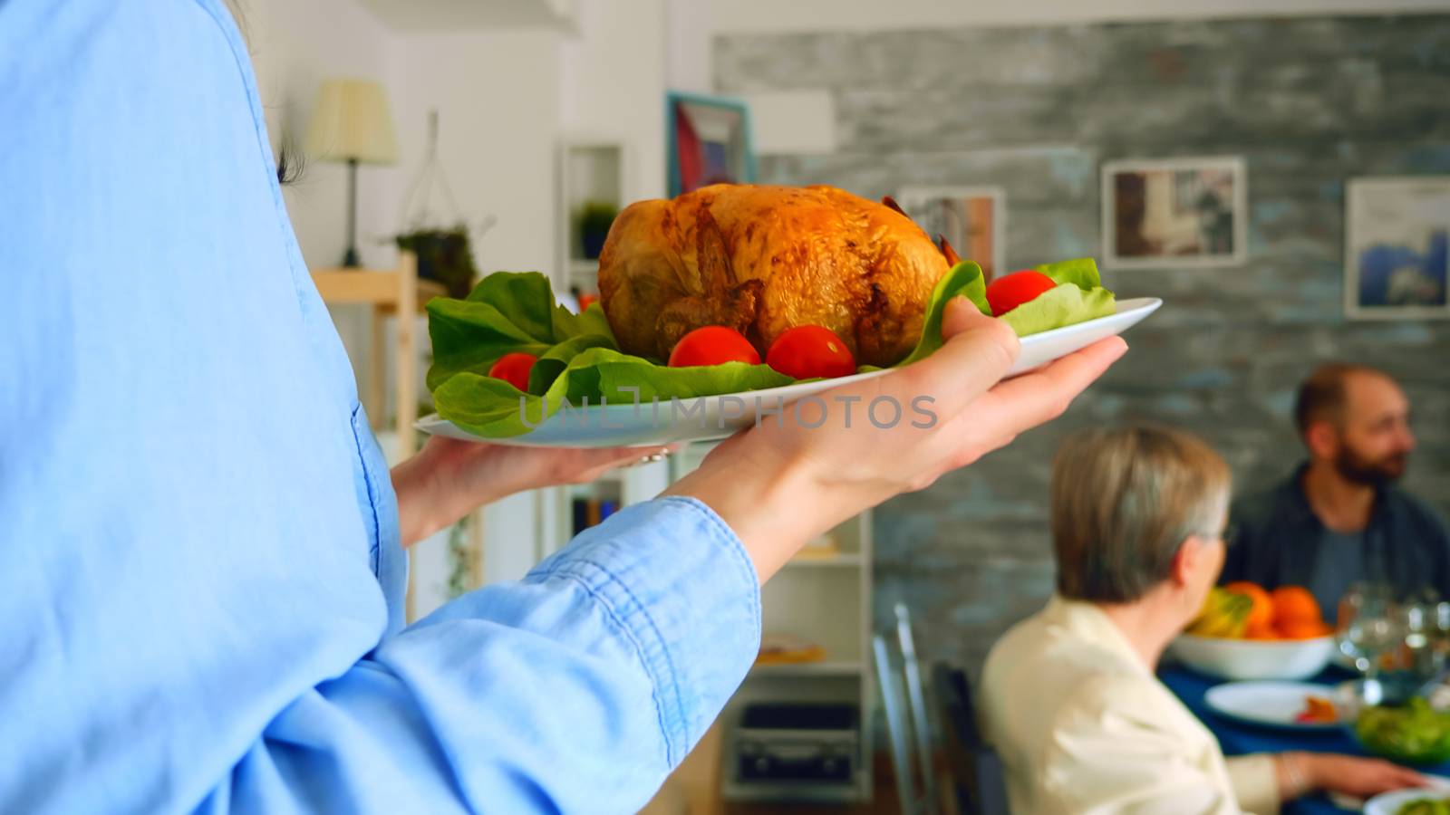 Follow shot of young woman with roasted chicken at family dinner.