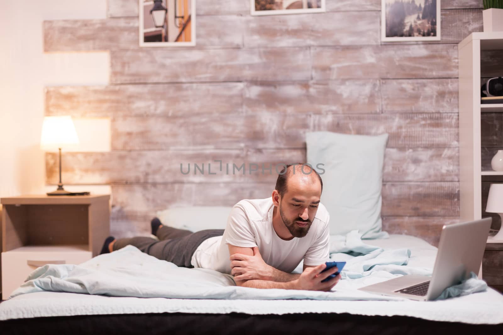 Man in bed at night wearing pajamas checking social media on smartphone.