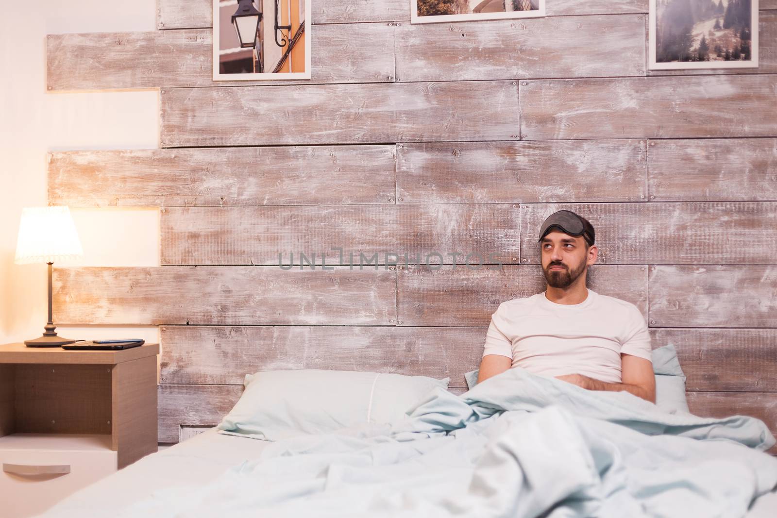 Tired man wearing a sleep mask in his big bed